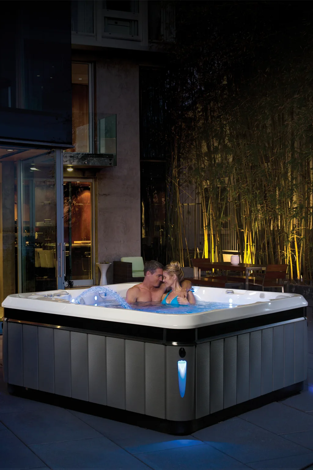 Couple relaxing in a Caldera hot tub on a lit patio at night