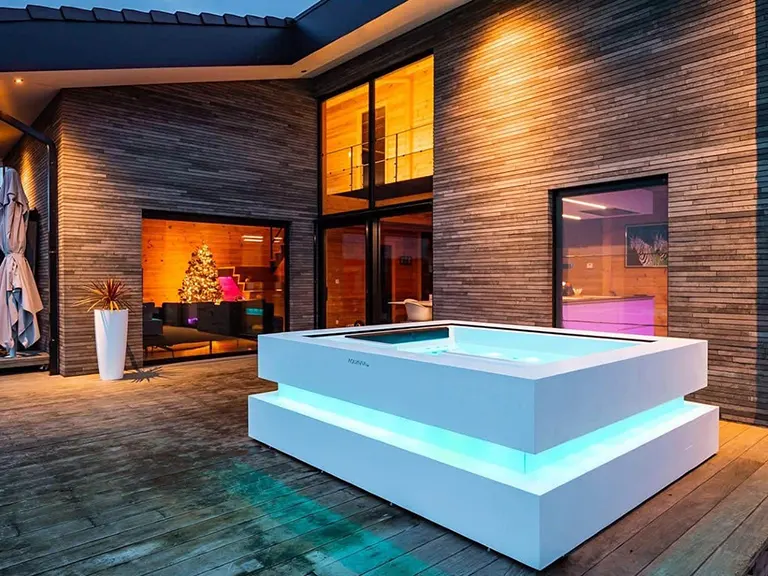 Aquavia Cube spa lit up on a stone terrace at dusk