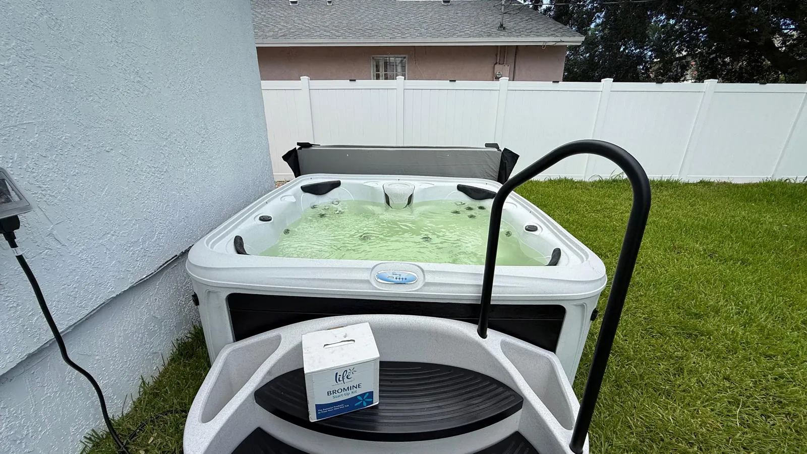 Plug-and-play hot tub beside the house with a handrail and step