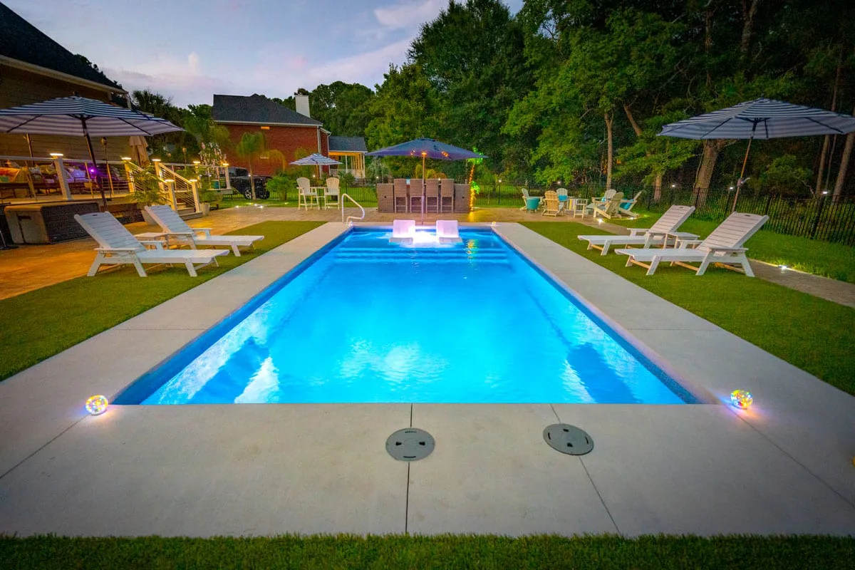 Latham Corinthian 12 fiberglass pool glowing blue at dusk with loungers