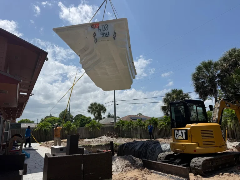 Fiberglass pool shell lifted by crane toward the excavation