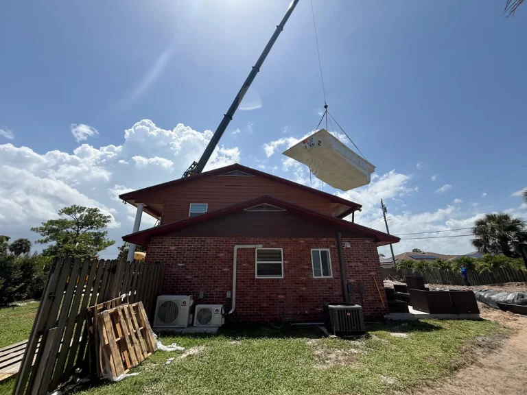 Fiberglass pool shell lifted by crane over a house