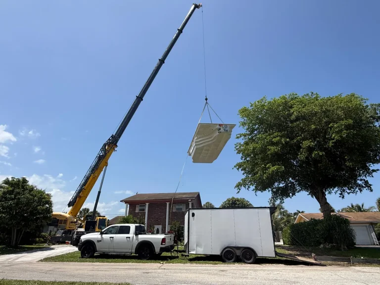Crane lifting a fiberglass pool shell from the street
