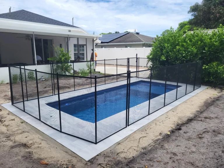 Compact fiberglass pool with a safety fence beside the patio