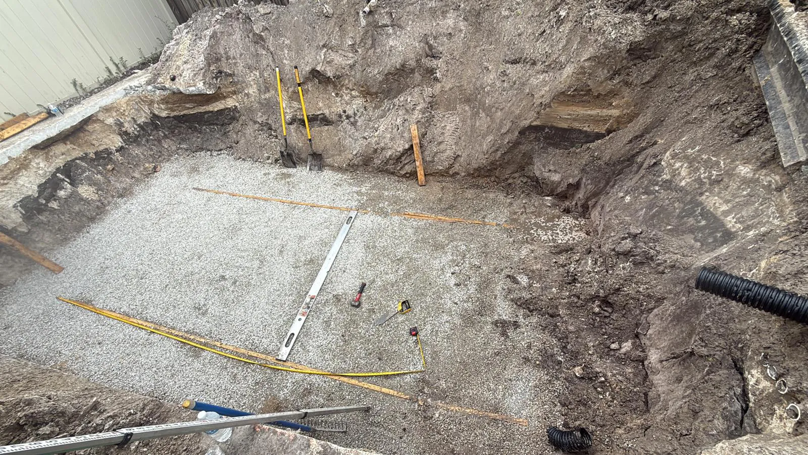 Excavation with a leveled stone base, a level and tape measures on it