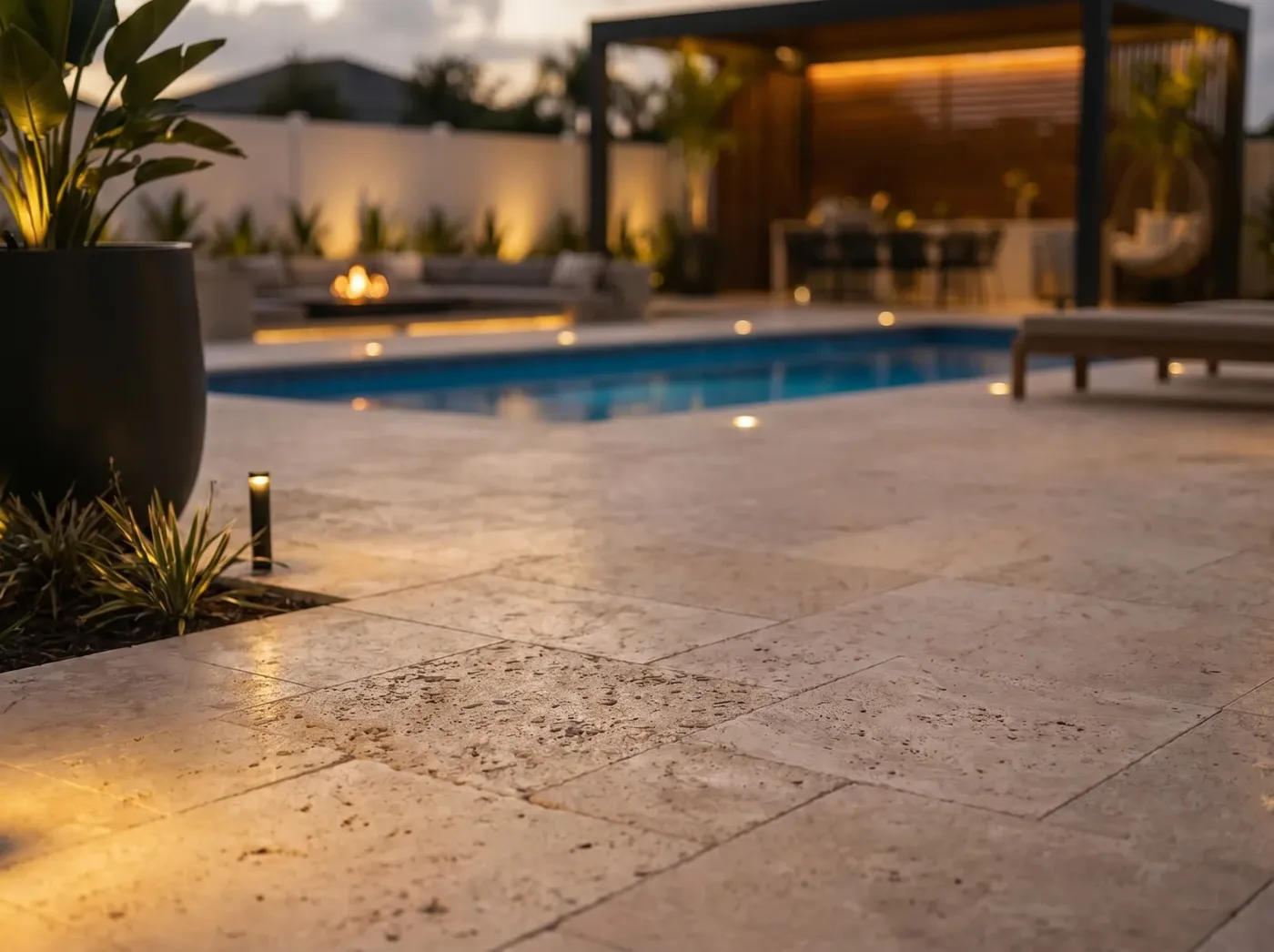 X-Pools Austin fiberglass pool lit at dusk beside a travertine terrace